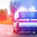 Ambulance driving on road with lights flashing.