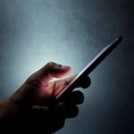 Hand holding a smartphone in dim light.