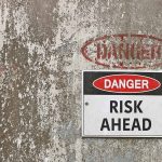"Danger: Risk Ahead" sign on weathered wall.