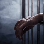 Hands gripping prison cell bars.