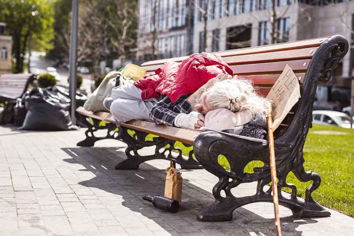 1100953052 featured image Person sleeping on park bench with cardboard sign.