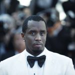 Man in white tuxedo with bow tie at event.
