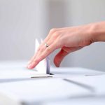 Hand placing paper in ballot box.