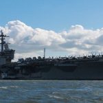Aircraft carrier on water under a cloudy sky.