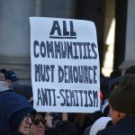 protesters holding handmade sign that says "all communities must denounce antisemitism"