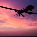 Silhouette of drone against colorful sunset sky.