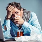 Sick person with laptop and tissues at desk