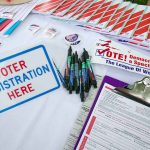 Voter registration table with forms, pens, and brochures.