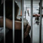 Person sitting behind bars in a dimly lit room