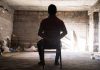 Person tied to chair in dimly lit room.