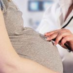 Doctor uses stethoscope on pregnant woman's belly.