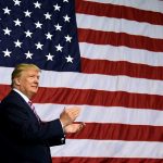 Man clapping in front of American flag backdrop