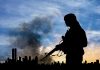 Silhouette of armed figure with smoky city skyline