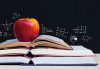 an apple sits on top of several open books with a chalkboard in the background