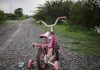 Pink children's bike with training wheels on gravel path.