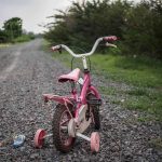 Pink children's bike with training wheels on gravel path.