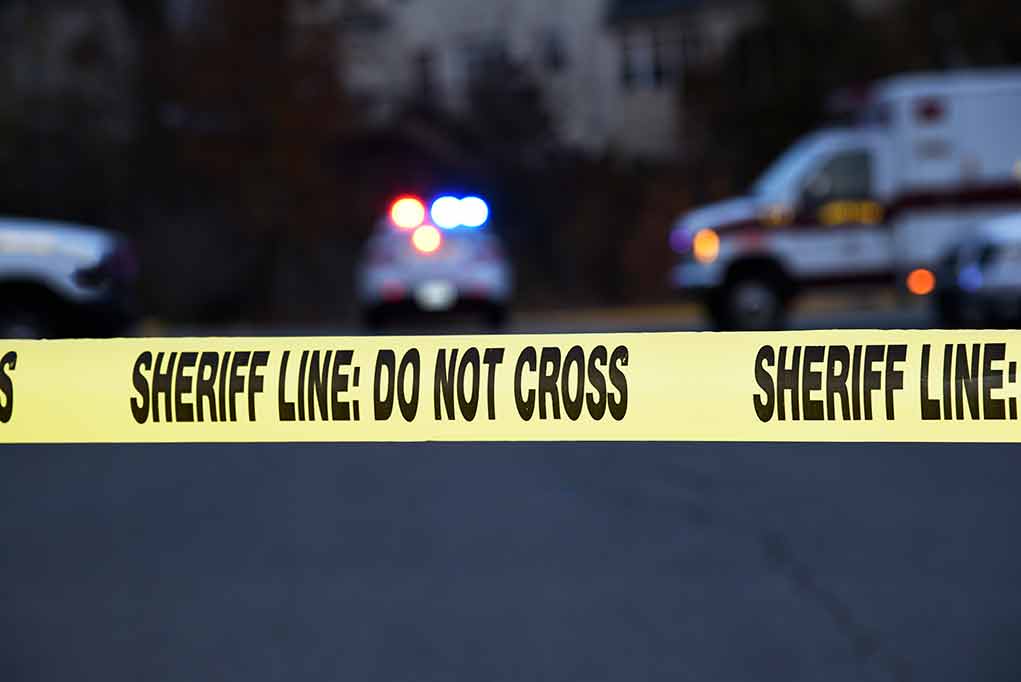 Sheriff line tape with emergency vehicles in background.
