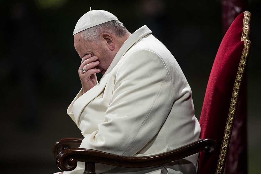Man in white coat sitting with head in hand