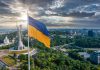 Ukrainian flag flying near city with statue monument