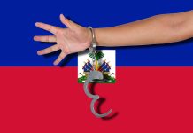 person's arm with handcuffs in front of the flag of Haiti