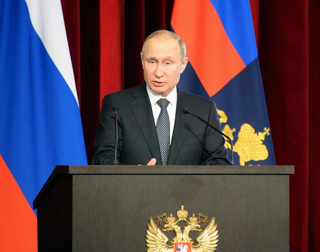 Man speaking at podium with flags behind him