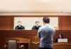 Man stands in courtroom before judges and stenographer