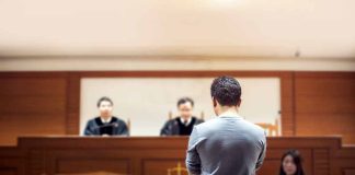Man stands in courtroom before judges and stenographer