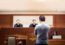 Man stands in courtroom before judges and stenographer