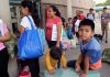 People waiting outside carrying bags boys sitting and playing
