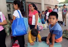 People waiting outside carrying bags boys sitting and playing
