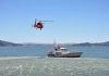 Helicopter flying above Coast Guard boat on water