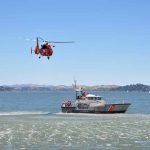 Helicopter flying above Coast Guard boat on water