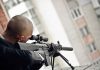 Person aiming a rifle from a building balcony