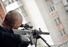Person aiming a rifle from a building balcony