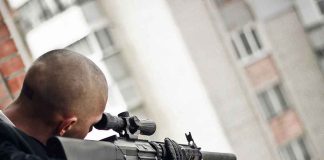 Person aiming a rifle from a building balcony