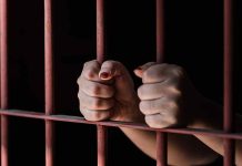 Hands gripping red jail bars tightly