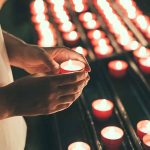 Hands holding a candle near several lit candles.