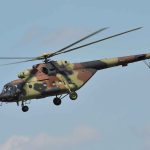 Camouflage military helicopter in flight against blue sky.