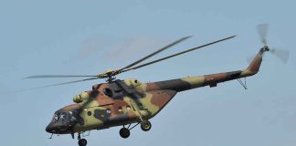 Camouflage military helicopter in flight against blue sky.
