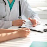 Doctor discussing with patient holding clipboard on desk