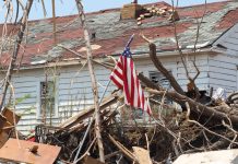 Damaged house with fallen tree and American flag