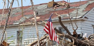 Damaged house with fallen tree and American flag