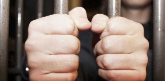 Hands gripping jail cell bars tightly