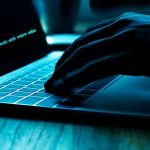 Hand typing on laptop with code on screen.