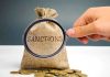 Hand holding magnifying glass over sack labeled Sanctions