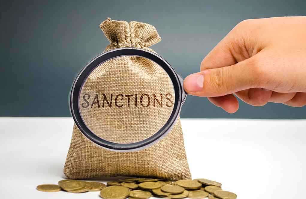 Hand holding magnifying glass over sack labeled Sanctions