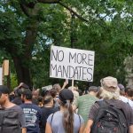 Crowd holds "No More Mandates" sign at protest.