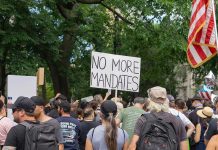 Crowd holds "No More Mandates" sign at protest.