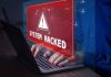 Warning sign "System Hacked" on laptop screen.