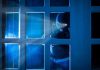 Masked figure peering through glass door at night